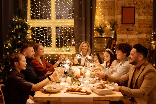 Free Family celebrating Christmas with dinner and sparklers, creating joyful holiday atmosphere indoors. Stock Photo