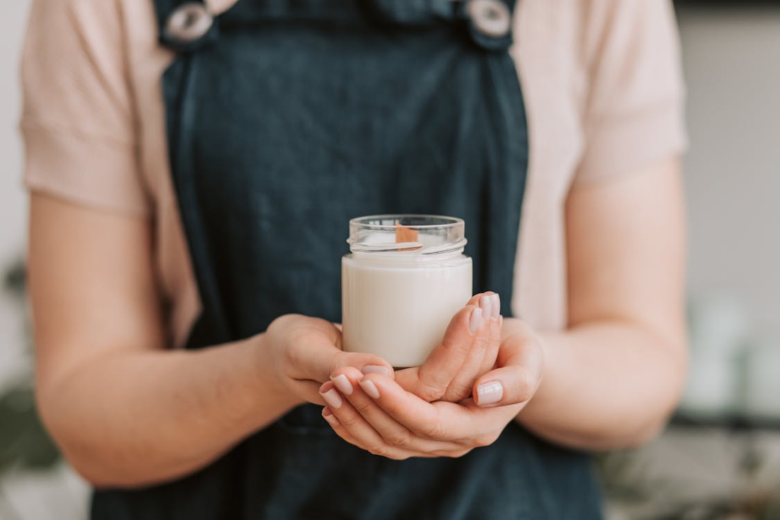 Free A close-up of a woman holding a handmade candle in a glass jar, showcasing small business crafting. Stock Photo