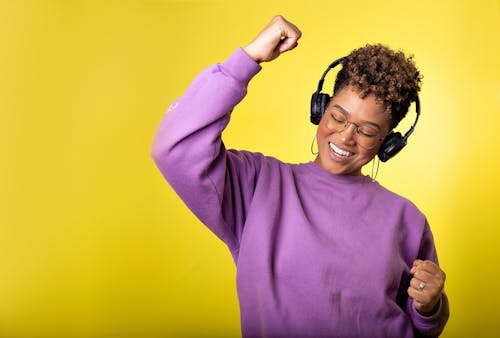 Free A cheerful woman with headphones enjoying music on a vibrant yellow background, expressing happiness and energy. Stock Photo