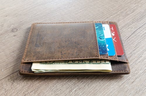 Free A brown leather wallet with cash and credit cards on a wooden surface. Stock Photo